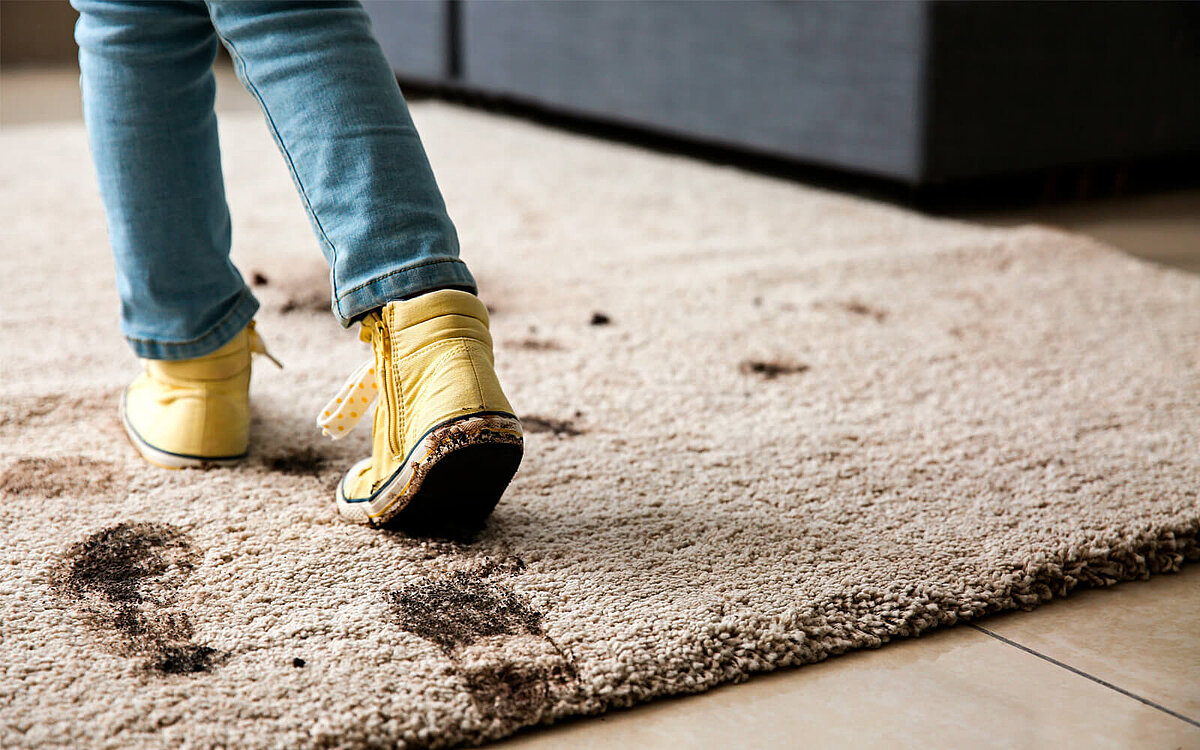 Ein Kind läuft mit dreckigen Schuhen über einen sauberen Teppich
