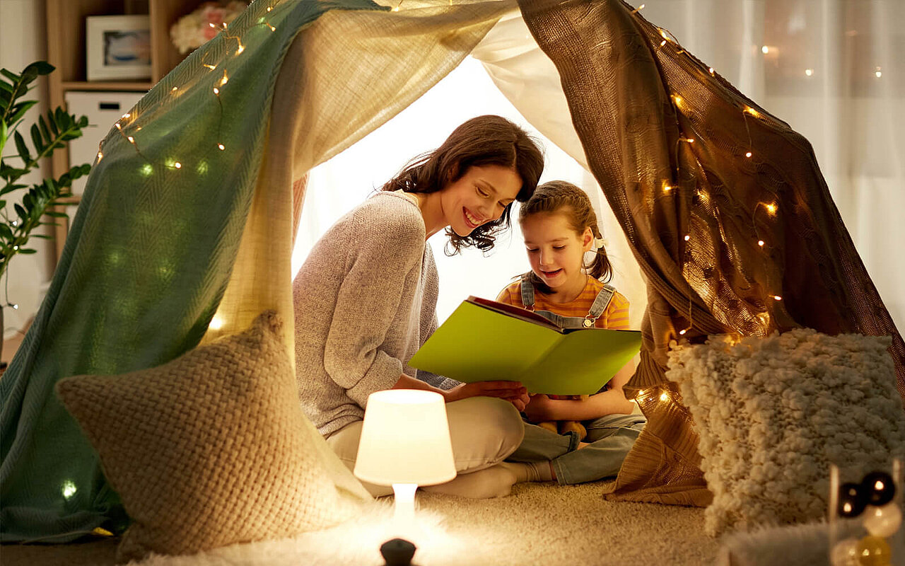 Mutter und Kind lesen ein Buch unter einem Zelt im Kinderzimmer