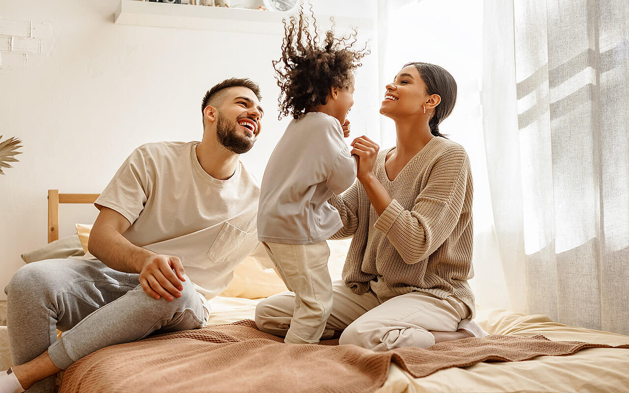 Eine Familie mit Kind tobt und lacht auf dem Bett
