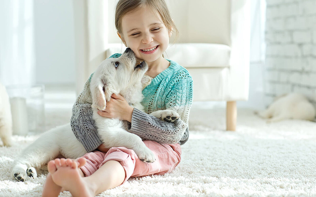 Ein Mädchen sitzt auf einem weißen Teppich und hat einen Hund auf dem Arm