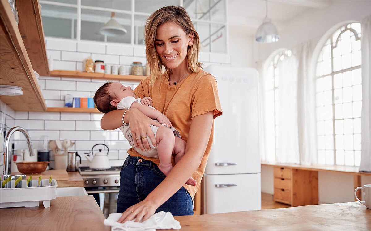 Eine Mutter hat Ihr Baby auf dem Arm und putzt die Küche