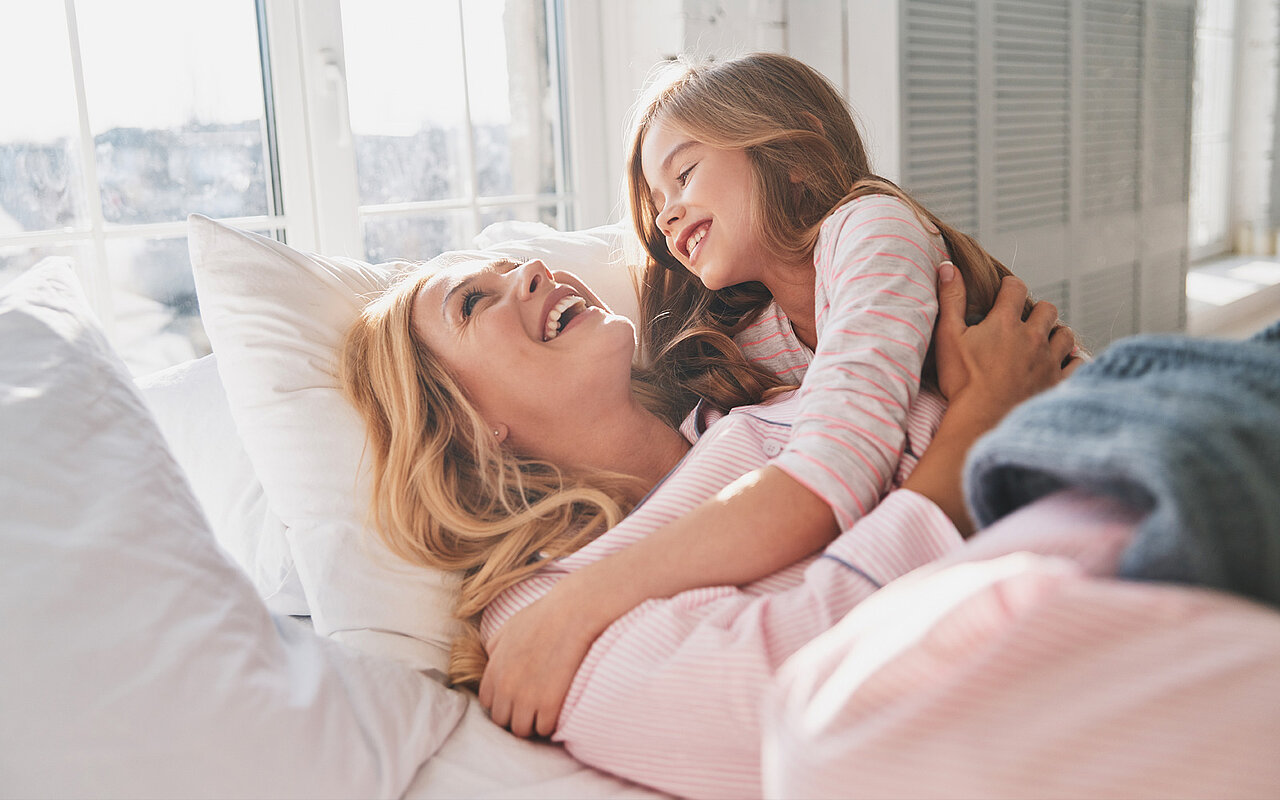 Eine Mutter im rosa Pullover kuschelt mit Ihrer Tochter im Bett 