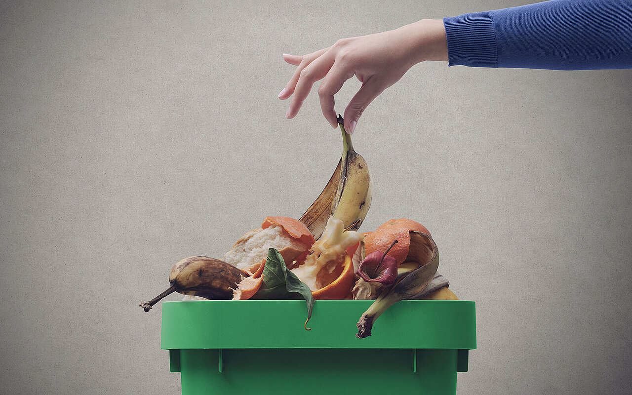 Eine Bananenschale wird in einen vollen Mülleimer gelegt 